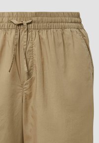 Hellbraune, elastische Hosen mit einem Kordelzugbund, seitlichen Taschen und einer glatten, leicht glänzenden Oberfläche.