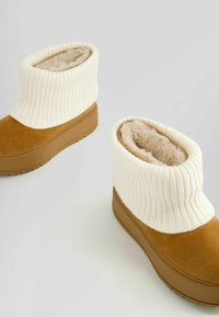 Tan-nahka kengät, joissa on pehmeä kerma-beige ribboitu varsike, fuzzy-vuori ja kiinteä ruskea pohja.