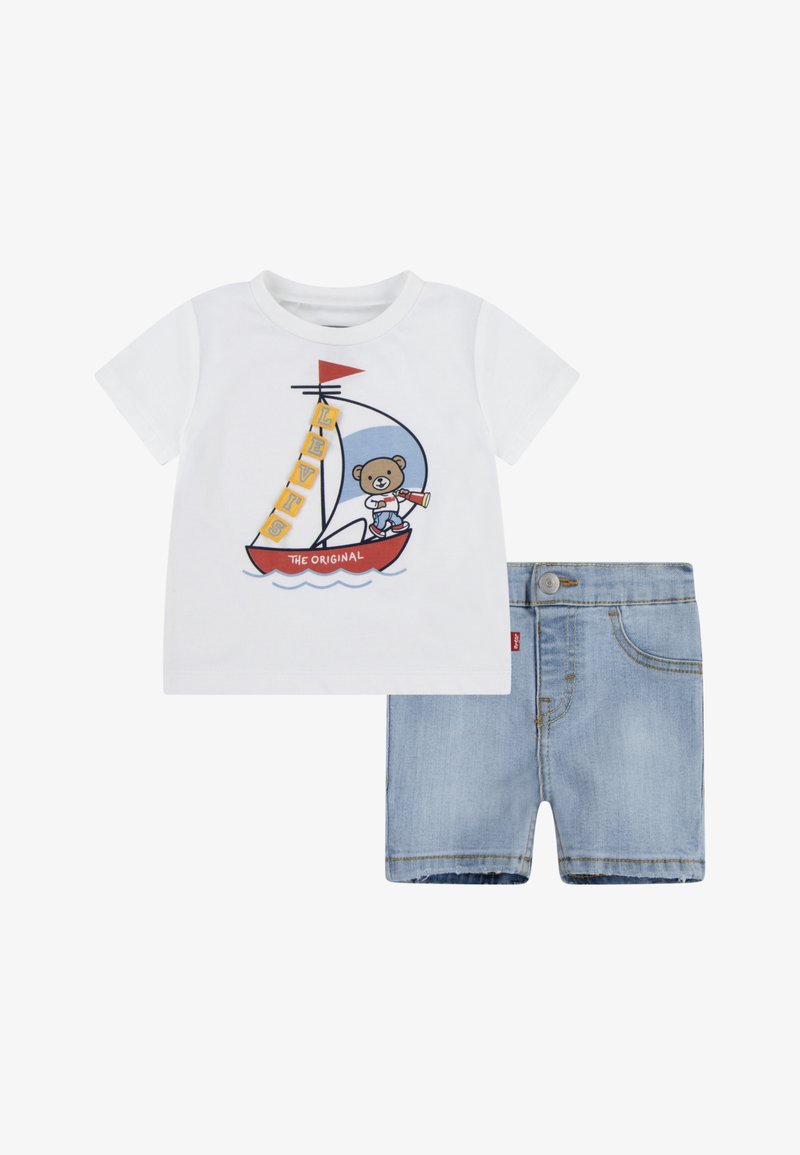 Camiseta de algodón blanca con un gráfico de un oso en un velero, combinada con unos pantalones cortos de mezclilla azul claro con un botón y bolsillos.