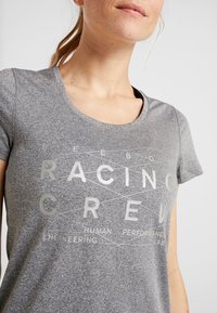 Camiseta gris de manga corta hecha de un tejido texturizado, con un diseño gráfico audaz que presenta las palabras "RACING CREW" en un estampado gris claro.