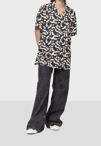 Camicia a maniche corte con motivo astratto nero e beige, abbinata a jeans di denim larghi e scuri e sneakers bianche.