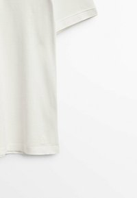 T-shirt med rund hals och kort ärm i off-white bomull, med en texturerad yta och en liten broderad logotyp vid fållen.