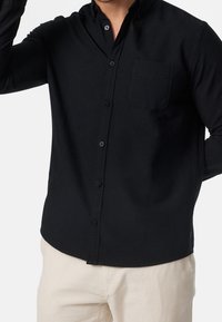 Czarna koszula na długi rękaw z guzikami, kołnierzykiem i pojedynczą kieszenią na piersi, wykonana z gładkiej tkaniny. Charakteryzuje się dopasowanym krojem i guzikami w tym samym kolorze.