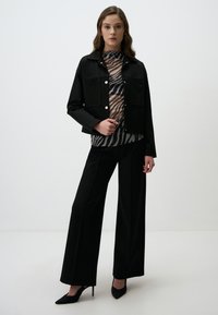 Zwarte cropped jas met twee grote zakken, gecombineerd met een top met zebra-patroon en wijde zwarte broek. Gedragen met zwarte hoge hakken.