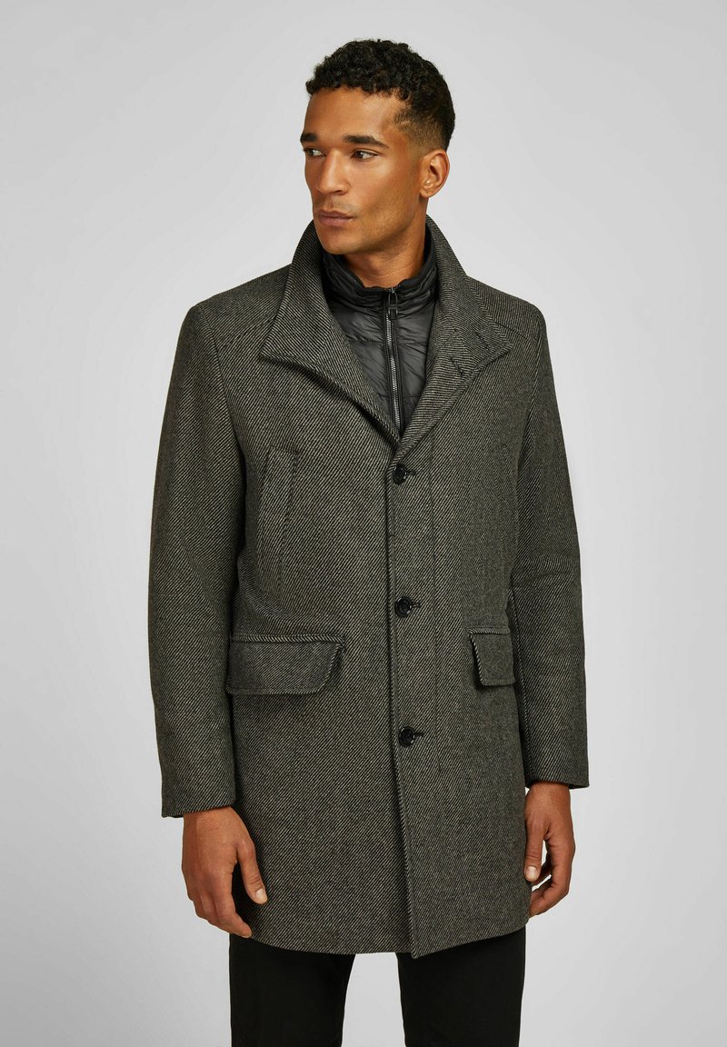 Wollmantel mit Fischgrätmuster in Dunkelgrau, breitem Kragen, vorderer Knopfverschluss und zwei vorderen Taschen. Innenjacke ist gefüttert und sichtbar.