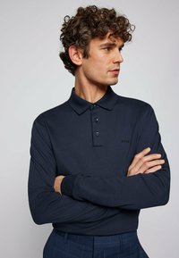 Navy long-sleeve polo shirt with a collar, three buttons, and a subtle logo. Fabric is smooth, with ribbed cuffs and a classic fit.