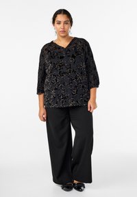 Čierny top s kvetinovým vzorom, s výstrihom do V, 3/4 rukávmi a mäkkou textúrou, kombinovaný so širokými čiernymi nohavicami a čiernymi topánkami.