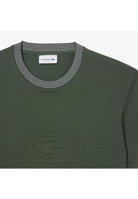 Donkergroene katoenen T-shirt met een ribgebreide gestreepte ronde hals. Voorzien van een reliëflogo en een gedetailleerd cirkelvormig patroon op de voorkant.