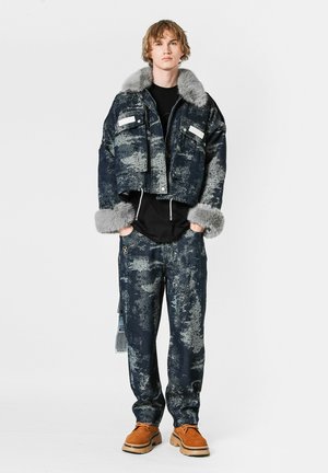 Chaqueta de denim recortada con cuello y puños de piel sintética gris, combinada con pantalones de denim oscuro a juego, ambos con patrones abstractos.