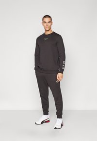 Dunkelgrauer Sweatshirt mit Logo, kombiniert mit passenden Jogginghosen. Verfügt über gerippte Bündchen und einen elastischen Taillenbund. Getragen mit weißen Sportschuhen.