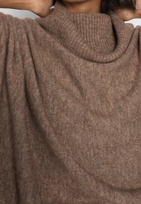 Poncho en maille marron avec un col cheminée côtelé et surdimensionné. Texture douce et tissu fluide, présentant une silhouette décontractée et drapée.