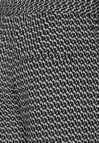 Černobílá látka s vzorem, která se vyznačuje geometrickým designem, s detailem bezešvé zadní kapsy. Materiál se jeví jako lehký a texturovaný.
