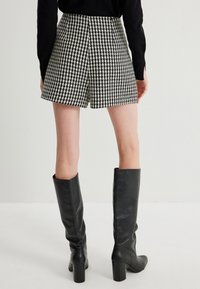 Houndstooth short met een zwart-wit ruitpatroon, met hoge taille en rechte snit, gecombineerd met lange zwarte leren laarzen.
