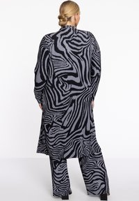 Langes, schwarzes und graues Zebra-Print-Outfit aus strukturiertem Material. Beinhaltet ein locker sitzendes Oberteil und weite Hosen, die mit vertikalen Streifen gestaltet sind.