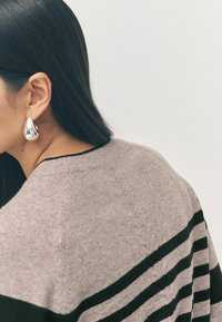 Pull gris avec des rayures noires, en mélange de laine, avec un col rond et une texture subtile. Présente également une boucle d'oreille en argent en forme de goutte.