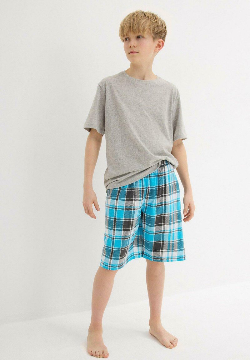 T-shirt gris et shorts à carreaux bleus avec des motifs turquoise, noir et blanc. Les shorts ont une taille élastique et sont de longueur genou.