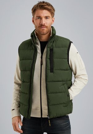 Green padded vest with a high collar, black accents, zippered chest pocket, and snap buttons. Worn over a textured beige sweatshirt.