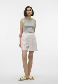 Grijze mouwloze top, lichtroze geruite shorts met een elastische tailleband en lichtgekleurde slide-sandalen met een knoopdetail.