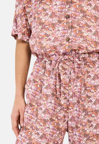 Bloemenoverall in roze, oranje en wit. Gemaakt van lichte stof met een relaxed fit, voorzien van een elastische taille en knoopdetails.