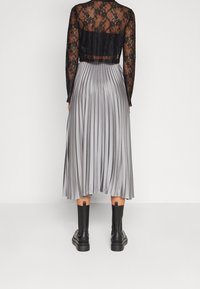 Černý krajkový top s dlouhými rukávy a zkráceným střihem, doplněný skládací stříbrnou midi sukní. K tomu patří černé boty po kotníky s mohutnou podešví.