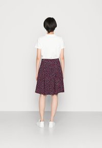 Falda navy con estampado floral y corazones rosa, diseño plisado y cintura elástica, combinada con una camiseta blanca de manga corta y zapatillas blancas.