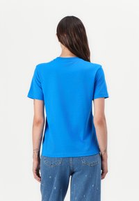 Tricou din bumbac albastru, cu mâneci scurte, guler rotund și o croială lejeră. Partea din spate are o textură netedă cu un design simplu.