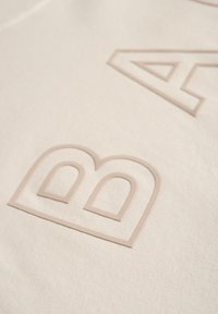 Kreemjas värvuses kangas, millel on lemmikloomakujulised heledad beežid kirjad geomeetriliste mustritega. Sile tekstuur koos peene läikega.