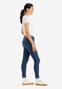 Tamno plave skinny traperice izrađene od denima, s srednjim strukom, suptilnim šavovima na stražnjim džepovima i smešnim kožnim oznakama na pojasu.