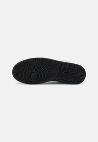 Black rubber sneaker sole with textured patterns, circular tread design, and prominent branding logo. Features grooves for grip and durability.