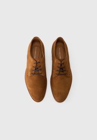 Zapatos de ante marrón con un acabado suave, que presentan una punta redonda, cordones oscuros en contraste y una plantilla de cuero con la marca.