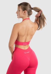 Roze activewear set met een halter crop top en high-waist leggings. Gladde textuur met subtiele branding op de tailleband.