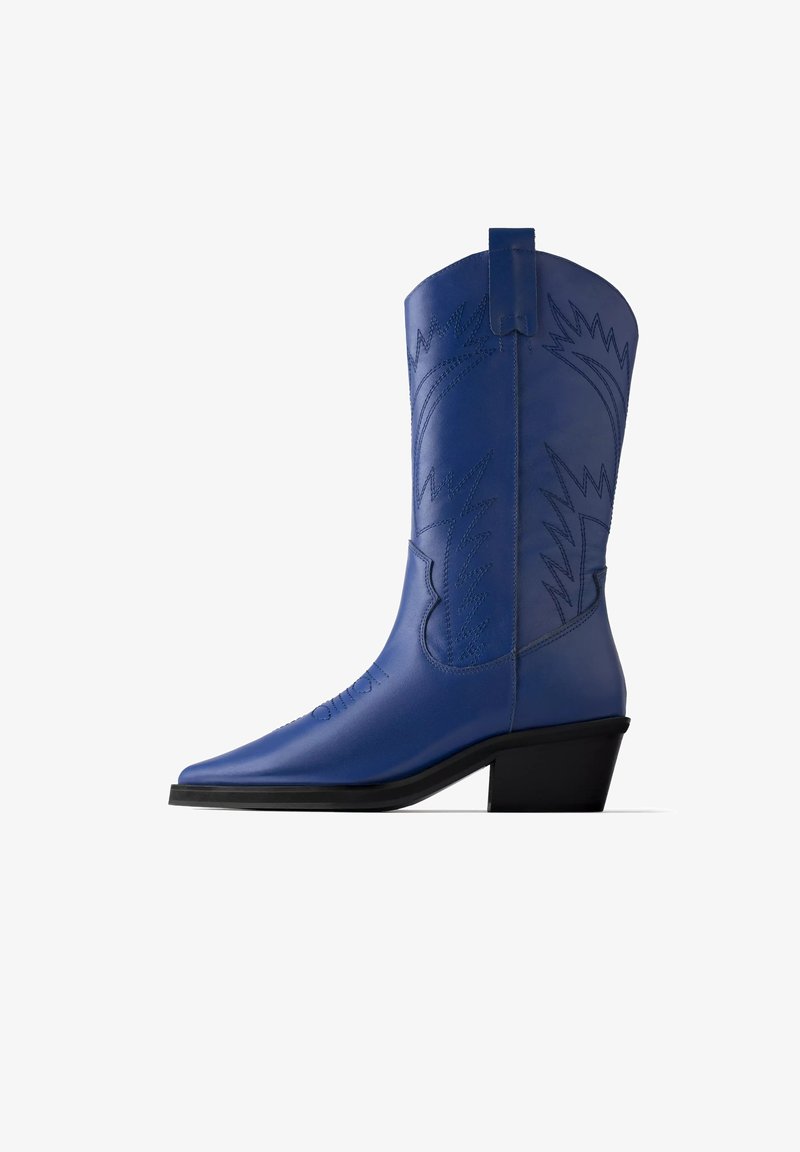 Botte de cowboy en cuir bleu avec bout pointu, talon noir incliné et coutures décoratives sur la tige et le pied, sur fond blanc.
