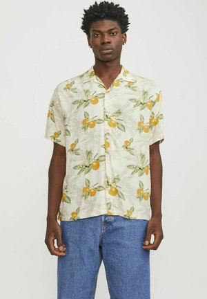 Camicia a maniche corte di colore crema chiaro con un motivo floreale arancione e verde. Presenta una vestibilità rilassata e una chiusura frontale con bottoni. Indossati jeans di denim sotto.