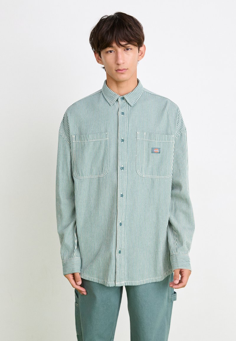 Striped button-up shirt in light green and white, featuring two chest pockets and long sleeves with cuffs. Made from lightweight fabric.