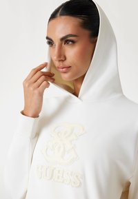 Witte hoodie met een zachte textuur, voorzien van een tonale geborduurde logo. De capuchon hangt soepel en de manchetten zijn geribbeld voor een strakke pasvorm.