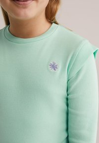 Mentaszínű, bordázott, hosszú ujjú ing, kerek nyakkivágással és egy kis lila virágos hímzéssel a mellrészen.