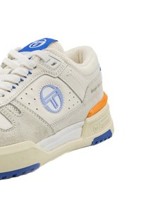 Beige Wildlederschuhe verfügen über ein blaues Logo, weiße Schnürsenkel und eine mehrfarbige Sohle mit orangefarbenen und blauen Akzenten, die über perforierte Details verfügt.