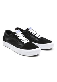 Une paire de baskets Vans noires avec des lacets blancs et des semelles en caoutchouc blanc épaisses, dotées de bouts en suede et de logos en rayures sur le côté.