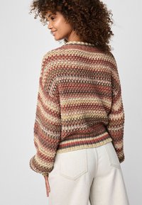 Pulover tricotat cu dungi multicolore în nuanțe de bej, rugină și maro. Are o croială lejeră, tiv ondulat și mâneci largi.