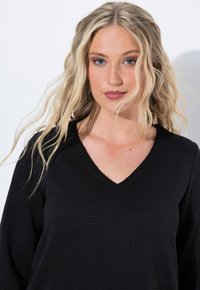 Top nero testurizzato con scollatura a V e motivi geometrici. Il tessuto presenta un design a coste, creando interesse visivo e profondità.
