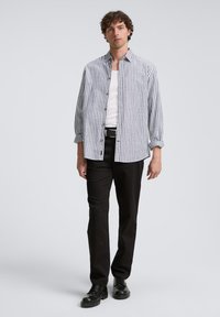 Chemise à rayures blanche et marine, avec une coupe décontractée, des manches longues et un ourlet arrondi, assortie à un pantalon et des chaussures noirs.