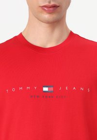 Crvena pamučna majica s okruglim izrezom, sa natpisom "TOMMY JEANS" i "NEW YORK CITY" ispod malog dizajna logotipa zastave.