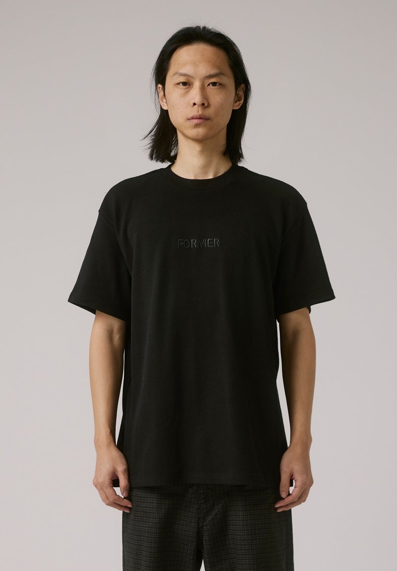 Black cotton t-shirt with short sleeves and a crew neckline. Centered embroidered text "FORMER" in a subtle finish. Relaxed fit, crew neck.