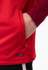 Rode sportieve shirt met een ritssluiting aan de zijkant, gemaakt van gladde stof; heeft een ronde halslijn en contrasterende kastanjebruine lange mouwen.