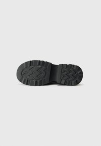 Black rubber sole with textured zigzag pattern, wide toe area, and raised edges for traction. Smooth finish with no visible branding.