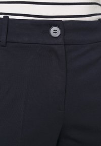 Geknoopte tailleband van navyblauwe broek, gedragen met een zwart-wit gestreept shirt.