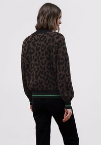 Hnědý svetr s leopardím potiskem, černým kontrastním límcem a manžetami, s zelenými akcentními pruhy na lemu, vyrobený z jemné tkaniny.