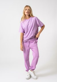 Violeta kokvilnas T-kreklis ar apaļu kaklu un brīvu piegriezumu, kombinēts ar atbilstošām sporta biksēm. Abi izstrādājumi ir aprīkoti ar elastīgiem auduma malām un patīkamu tekstūru.