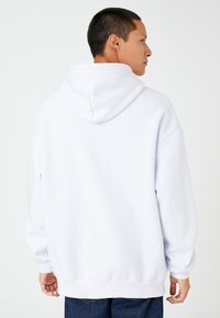 Biała bluza z kapturem, wykonana z miękkiego materiału, z dużym kapturem, opadającymi ramionami oraz ribbowymi mankietami i dołem. Prosty i minimalistyczny design.