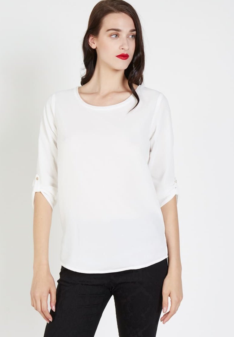 Blusa blanca de manga larga con escote redondo. Presenta mangas enrollables aseguradas con botones. Está hecha de una tela suave y ligera.